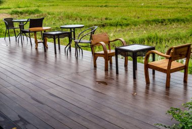 Eski tarz tahta sandalyeler ve ahşap teras zemininde cam masa.