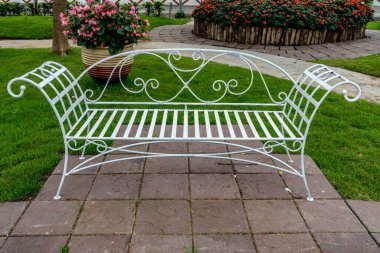 Bahçenin beton zemininde beyaz metal park bankı