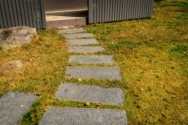 Beton blok yolu ve parkta gri ahşap çitli yeşil çimen.