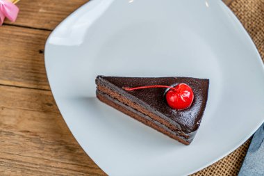 Beyaz seramik tabakta kırmızı kirazlı bir parça çikolatalı pasta.