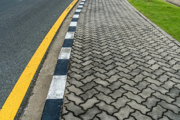 Asphalt road with yellow line curve and concrete block sidewalk