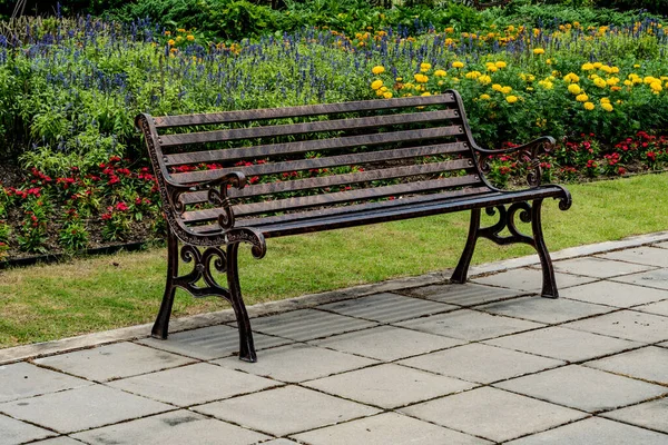 Iron park bench on concrete floor in colorful flowers garden