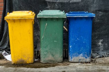 Beton zeminde yeşil ve sarı çöp tenekesi