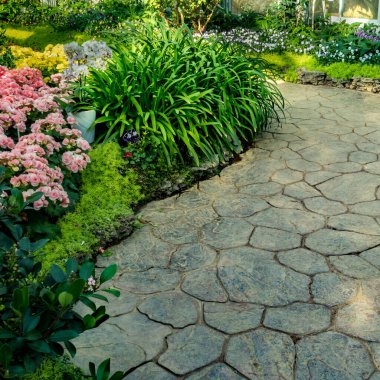 Parktaki beton yol renkli çiçekler ve yeşil bitkilerle dolu.