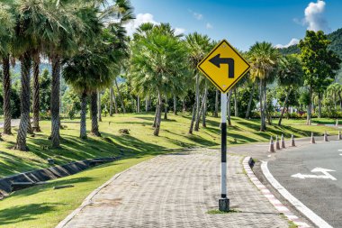 Sarı Sola dön kaldırımdaki trafik işaretinden mavi gökyüzü arkaplanındaki parkta