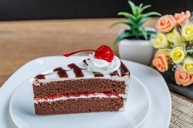 Beyaz kremalı çikolatalı pasta ve beyaz seramik tabakta kırmızı kiraz.