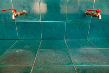 Yeşil kiremitlerin üzerindeki paslanmaz musluk sırası beton duvar