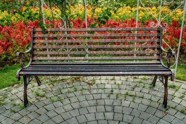 Renkli çiçeklerin bahçesinde beton zeminde demir parktaki bank