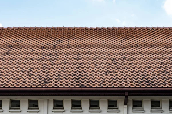 Old brown clay tiles roof pattern with small windows on concrete wall