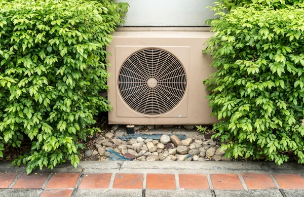 Side of air condition condenser unit between green leaves