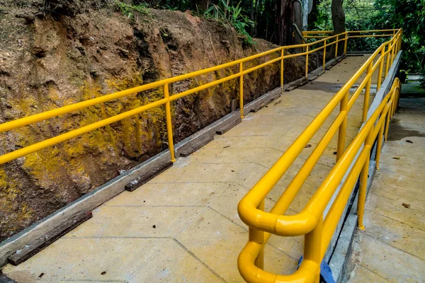 Concrete ramp for wheelchair with yellow iron railing in the park