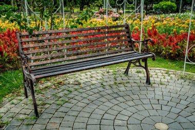 Renkli çiçeklerin bahçesinde beton zeminde demir parktaki bank