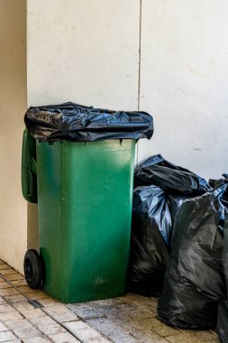 Beton zeminde siyah plastik torba olan yeşil çöp tenekesi