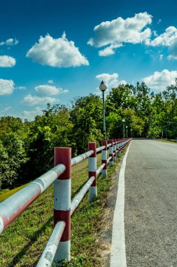 Mavi gökyüzü arka planında kırmızı ve beyaz çitli asfalt yolu perspektifi