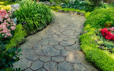 Parktaki beton yol renkli çiçekler ve yeşil bitkilerle dolu.