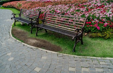 Parkta renkli çiçekleri olan metal park bankı