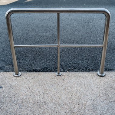 Beton zeminde asfalt yol arka planında paslanmaz parmaklıklar var.