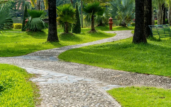 Parkta yeşil çimenler olan taş beton yol.