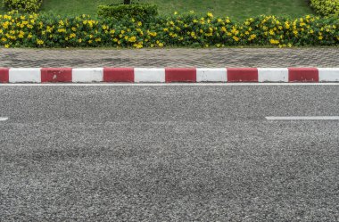 Asfalt yolu kırmızı ve beyaz beton kaldırım ve sarı çiçeklerle