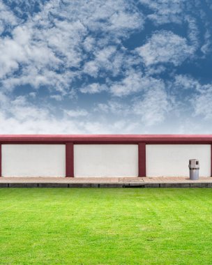 Mavi gökyüzü arka planlı yeşil çimenli beton çit