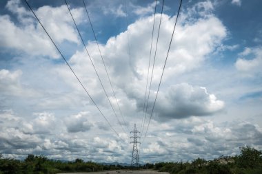 Yüksek voltajlı elektrik hatları ve beyaz bulutlar ve mavi gökyüzü üzerindeki pilon
