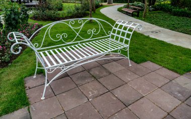 Bahçenin beton zemininde beyaz metal park bankı