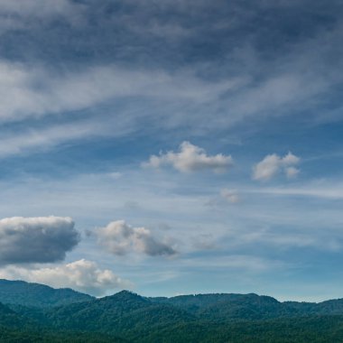 Mavi arka planda beyaz bulutlu dağ ve orman