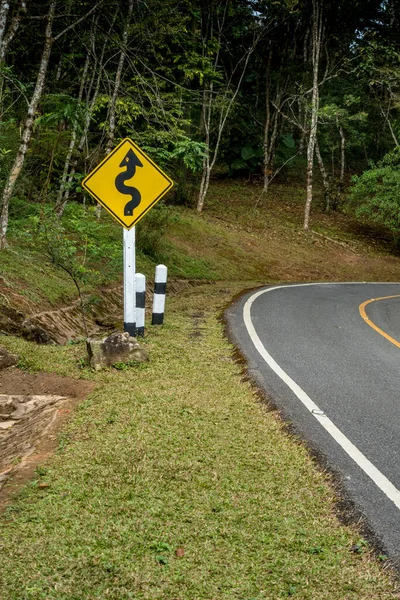 Yellow curve road sign on the road to the jungle