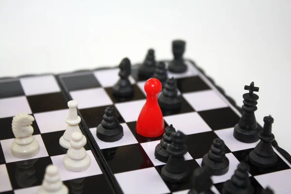 Siyah beyaz satranç taşları ile satranç tahtası üzerinde kırmızı ludo heykelcik. Benzersiz sıradışı fikirler, liderlik, iş konuları kavramı. — Stok fotoğraf