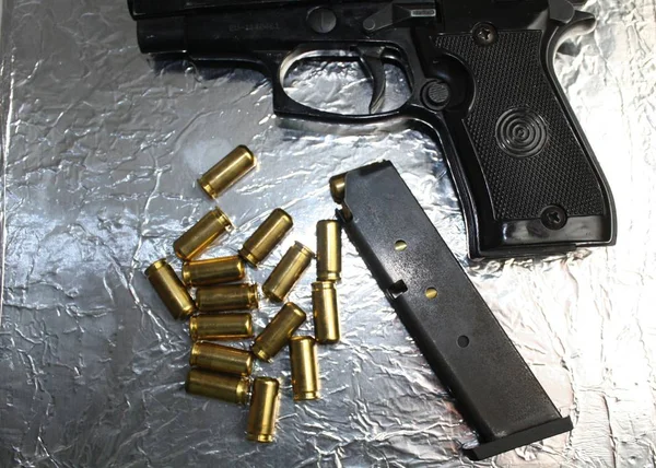 Pistola e balas de latão na superfície brilhante prata — Fotografia de Stock
