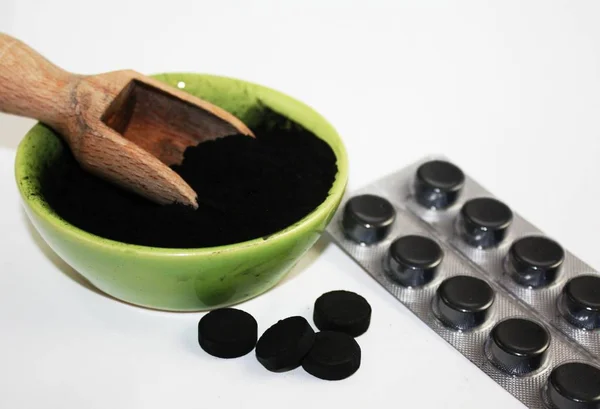 Aktivált szén fekete tabletták és por tálban fehér háttér Stock Fotó