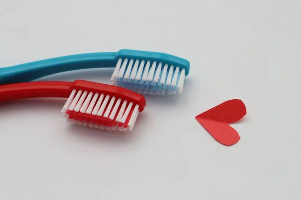Duas escovas de dentes nas cores vermelha e azul e um papel vermelho forma simbólica coração. Conceito de amor . — Fotografia de Stock