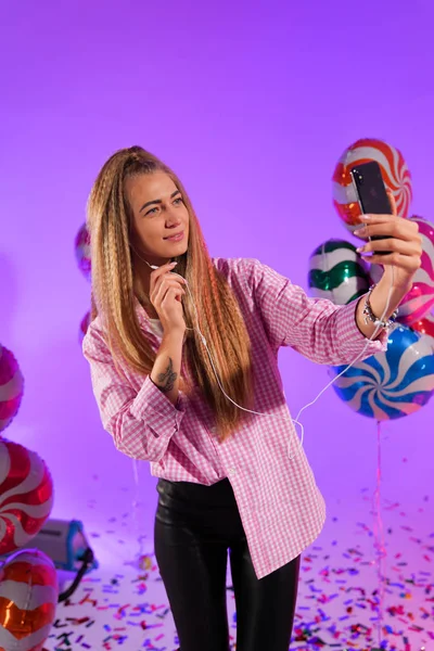 Girl in headphones with a smartphone, sings a song, on a purple background of candy, colored balloons