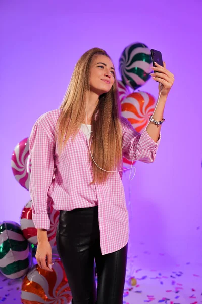 Girl in headphones with a smartphone, sings a song, on a purple background of candy, colored balloons