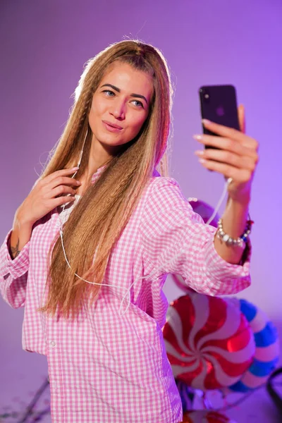 Girl in headphones with a smartphone, sings a song, on a purple background of candy, colored balloons