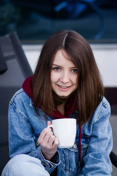 smiling girl in a denim jacket with a white mug