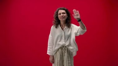 Kıvırcık kız el sallıyor, hoş geldin diyor kırmızı bir arka plan gülüşü