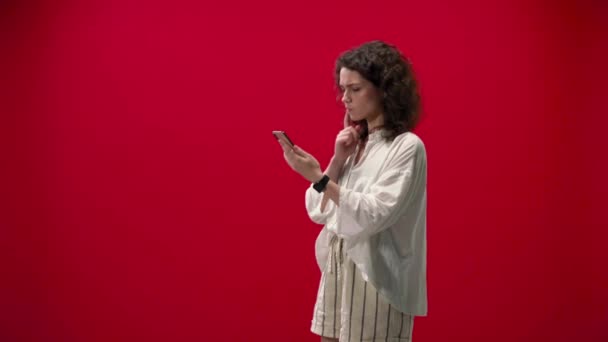 巻きガールは赤い背景に手でIphone 11Proでゲームをプレイする — ストック動画