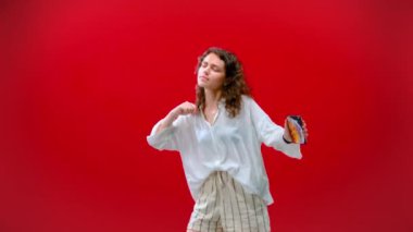 Kıvırcık Kız kırmızı arka planda elinde iPhone 11pro ile dans ediyor.