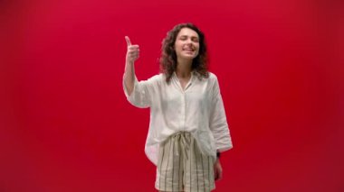 Kıvırcık kız sevinir ve kırmızı arka planda serinkanlılığını gösterir. Başarılı ve tatmin olmuş.