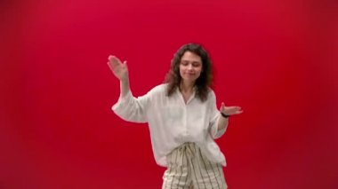 Kıvırcık Kız kırmızı arka planda elinde iPhone 11pro ile dans ediyor.