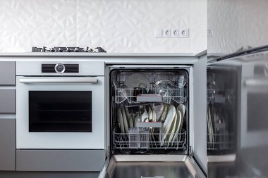 Açılan bulaşık makinesi içinde yemekleri ile sadece yıkanmış gri cephede ve beyaz duvar olan bir mutfak.