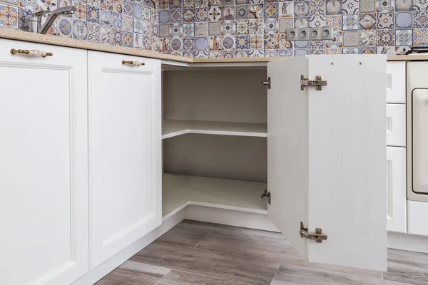 Solution for a kitchen corner in a cupboard. The angular opening with corner hinges. Classical kitchen interiors and white wooden fronts.