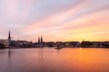 Hamburg'da gün batımı. Alster Gölü, Hamburg Rathaus görünümüne ve göl merkezinde kurulu bir Noel ağacı dekore edilmiş şehir merkezinin panoramik görünümü. Atmosfer yeni yıl.