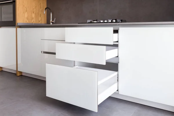 Opened kitchen drawer, kitchen in a modern loft style with wooden elements, grey countertop and backsplash.