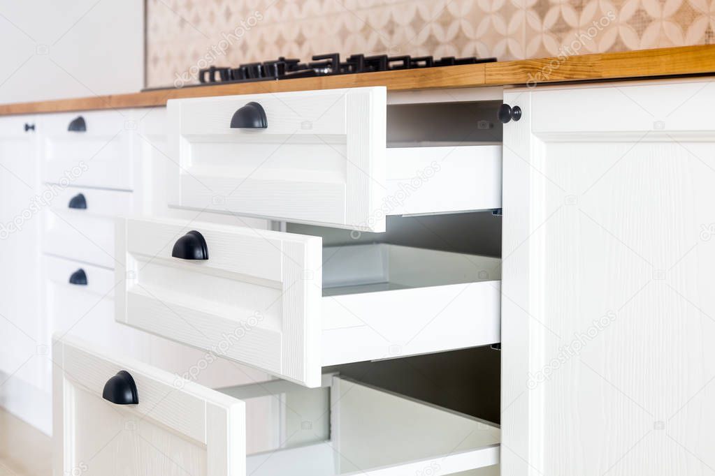 Opened kitchen drawers, kitchen in a traditional style with wooden white facade, black handles and wooden countertop 