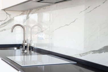 Siyah kuvars tezgah ve mermer kiremit backsplash ile beyaz parlak mutfak yakın. İnşa-gizli kaput ve undermonte lavabo. 