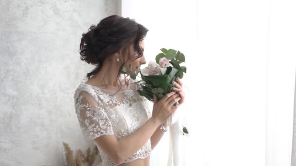 新娘穿着华丽的白色婚纱和鲜花站在窗口附近 — 图库视频影像
