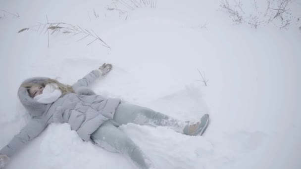 快乐女人享受美好的冬日 躺在雪地上和移动手臂 — 图库视频影像