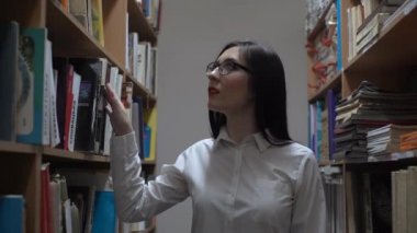 4k Genç Kadın Kütüphanede Bir Kitap Seçer. Boo'nun arasındaki koridorda.
